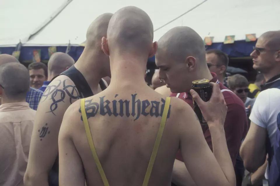 英国，1990年。参加同性恋骄傲游行的男同性恋光头党人，其中一人的背上纹有“光头党”（skinhead）字样。