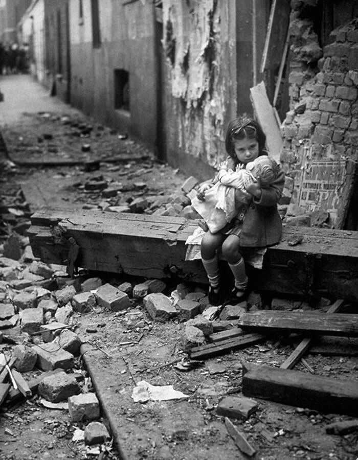 1940年，伦敦。一个小女孩坐在她那被炸毁的家园废墟中，怀里抱着她的玩偶。