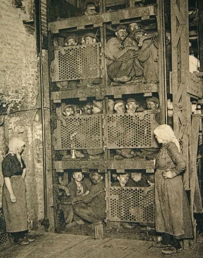 这是一张摄于1900年左右（可能在比利时）的照片，画面中一群煤矿工人（包括成年男性，也可能有未成年男孩）正挤进一座“升降吊笼”，准备下井进入煤矿。