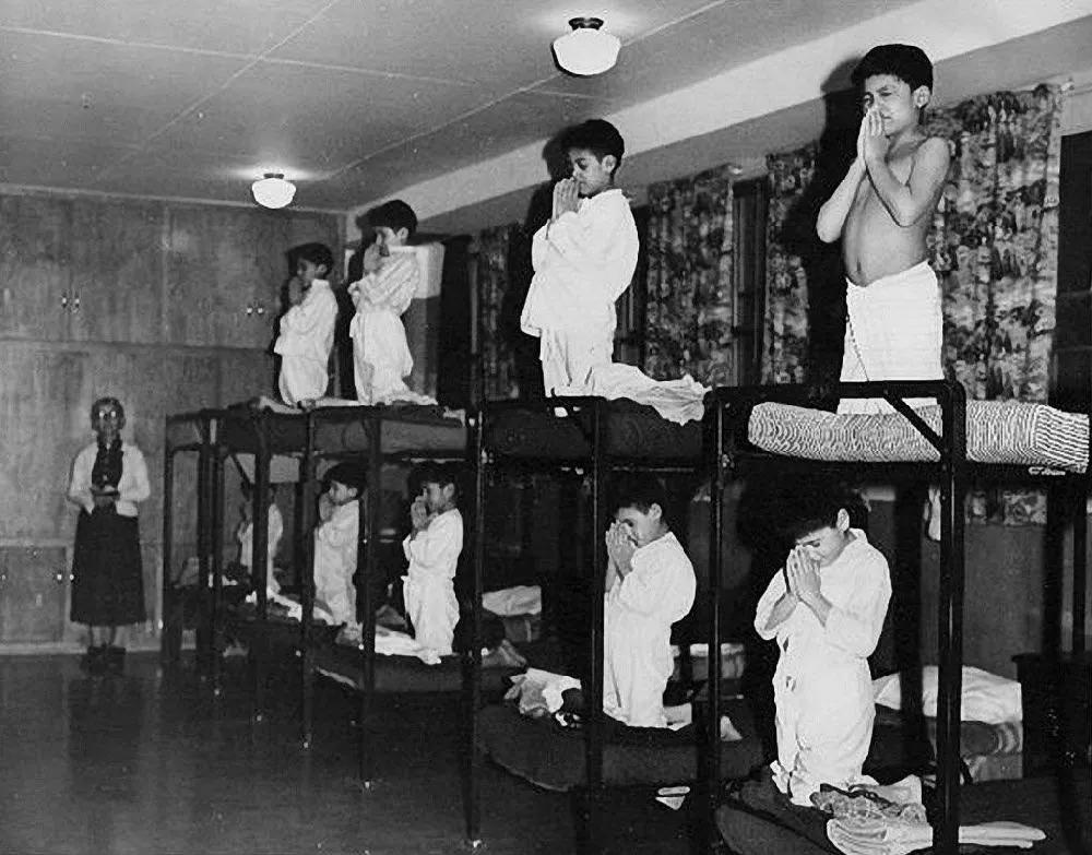 Indigenous children forced to pray to god in a residential school ran by the Canadian government and Catholic Church between 1930 and 1970, unknown location [1000 x 783]